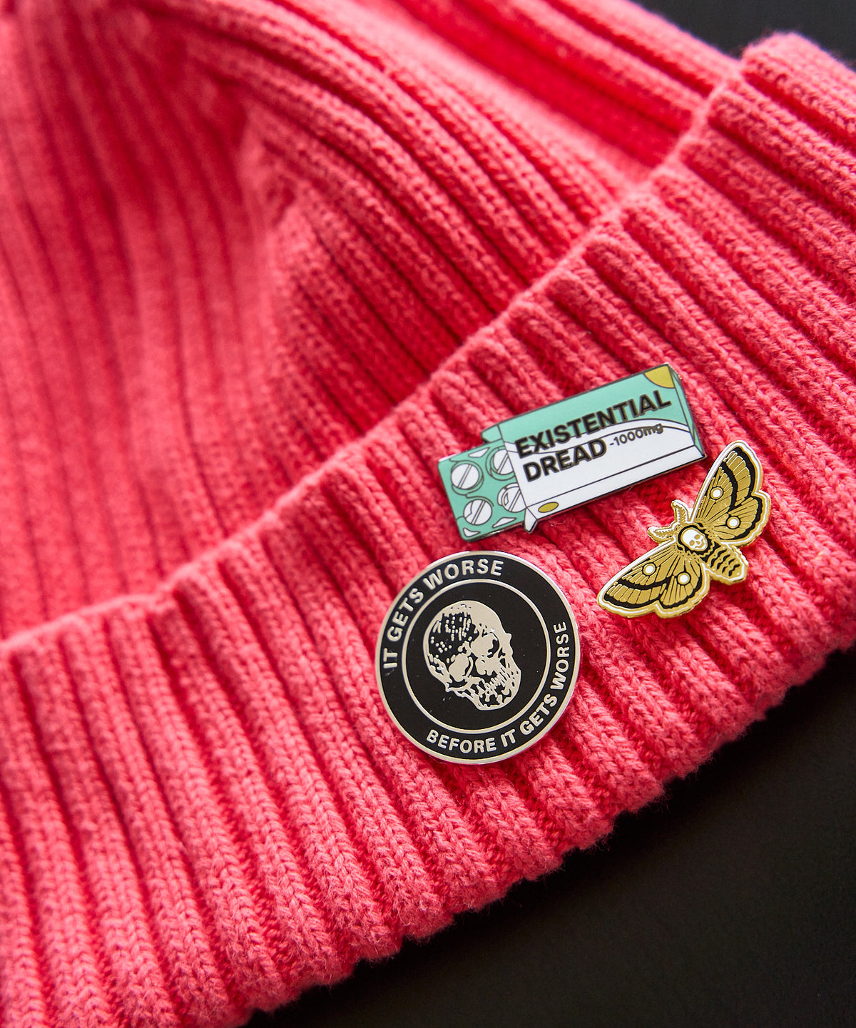 Death's Head Moth pin worn on a red knit beanie alongside other Strike Gently pins