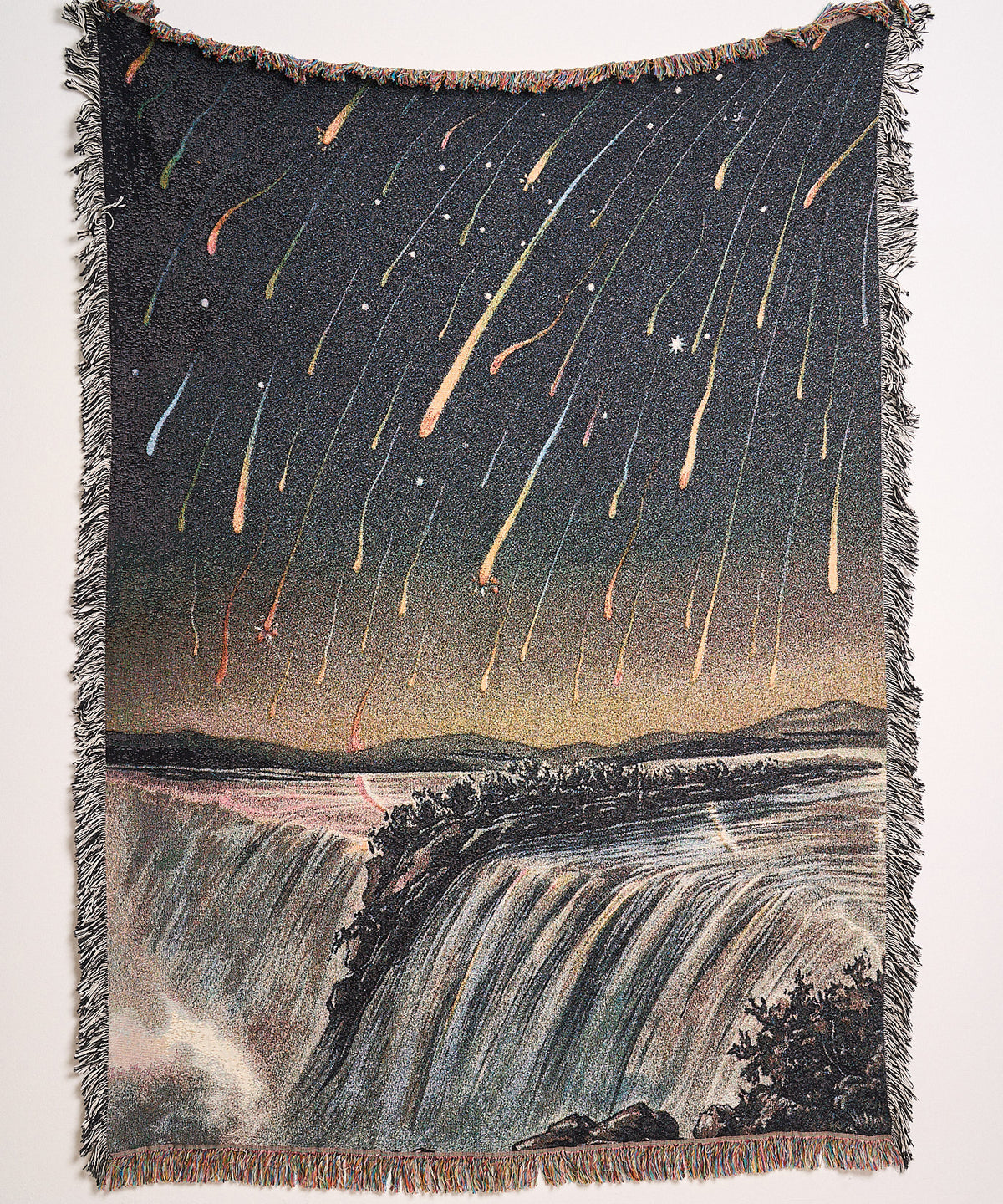 Meteor Shower woven blanket hanging on a wall, showing meteors streaking over a waterfall at night