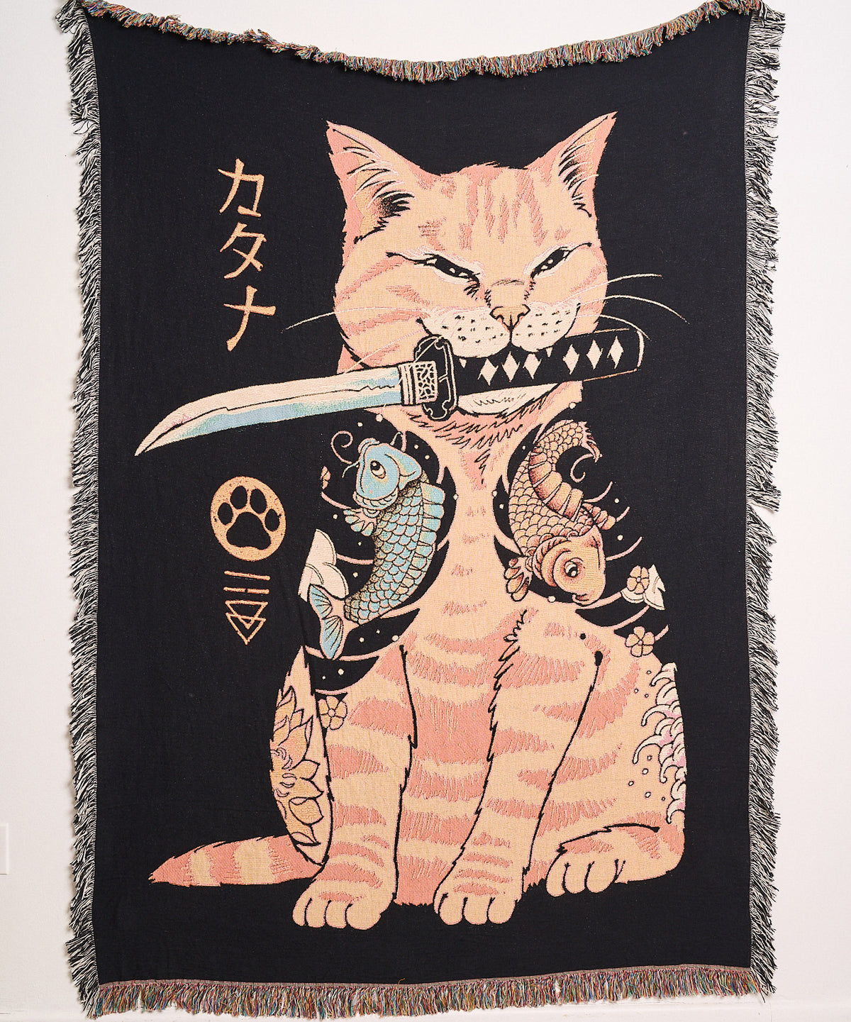 Cat / Knife woven blanket hanging on a wall, showing a tattooed tabby cat holding a katana in its mouth