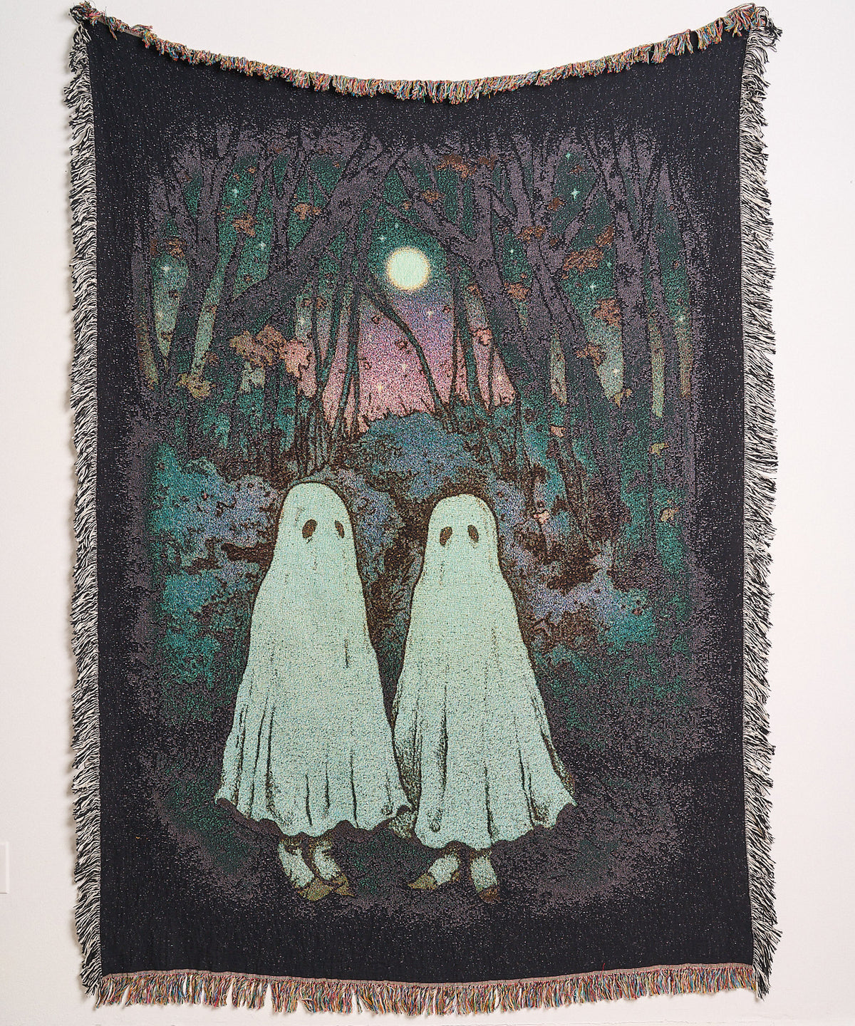 Ghost Pals woven blanket hanging on a wall, showing two sheet ghosts walking through a dark forest under a full moon