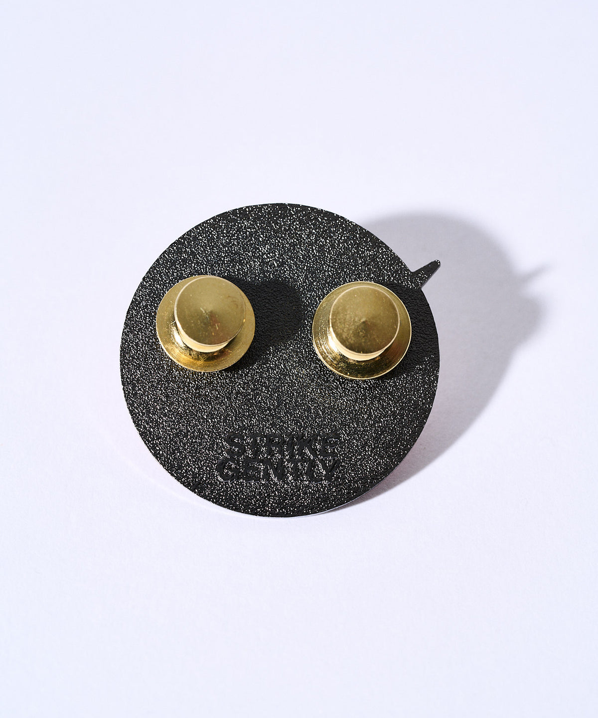 Back of the Ungovernable pin showing the black backing, two gold clutches and Strike Gently backstamp