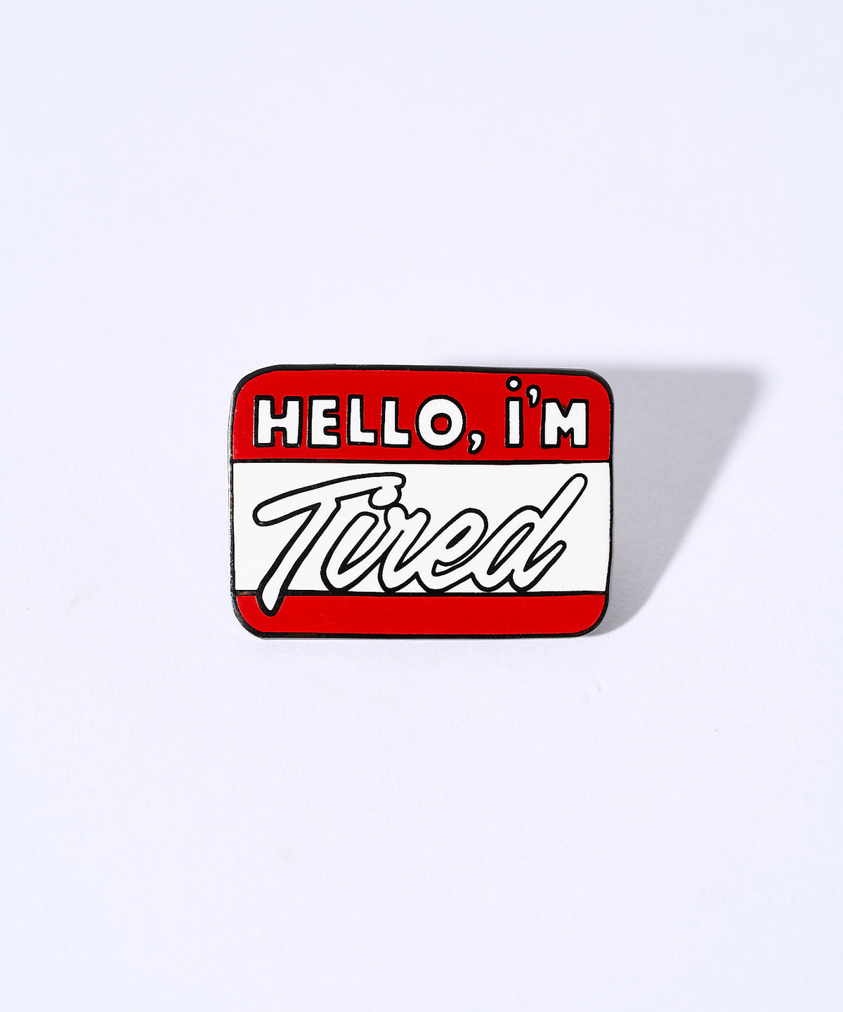 Hello, I'm Tired enamel pin, a red and white name tag design, on a lavender background