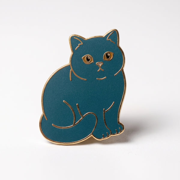 Blue Cat enamel pin, a chubby slate-blue shorthair cat with amber eyes sitting with its tail wrapped around