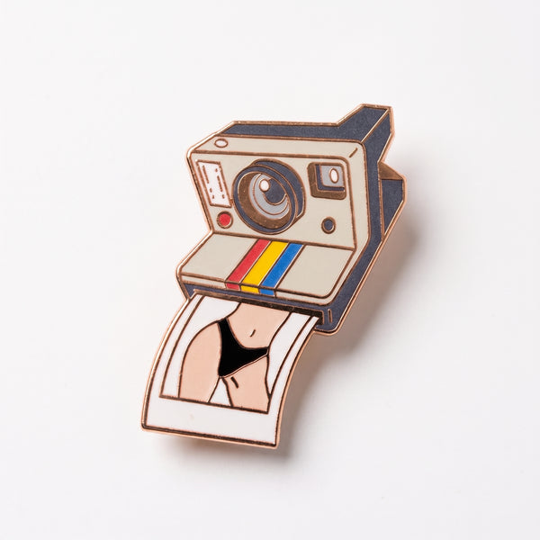 Instant Camera enamel pin, a cream retro instant camera with a rainbow stripe printing a cheeky bikini photo