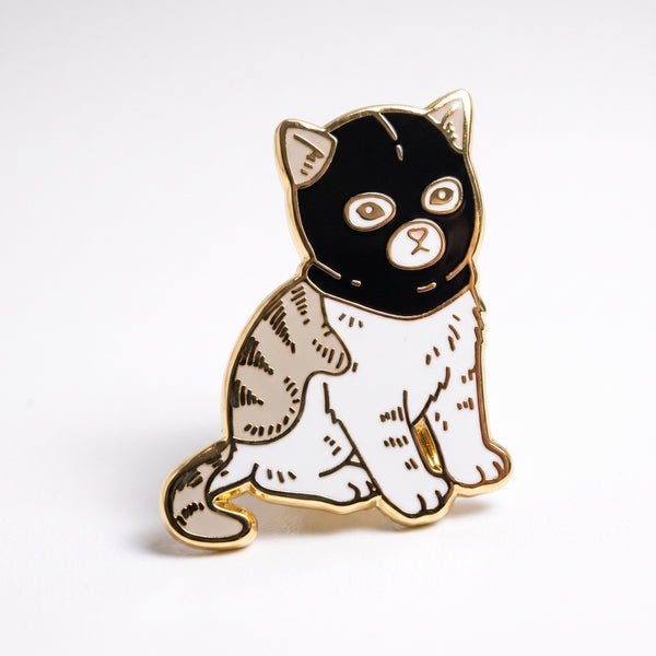 Cat Ski Mask enamel pin, a white and gray tabby cat sitting upright wearing a black ski mask