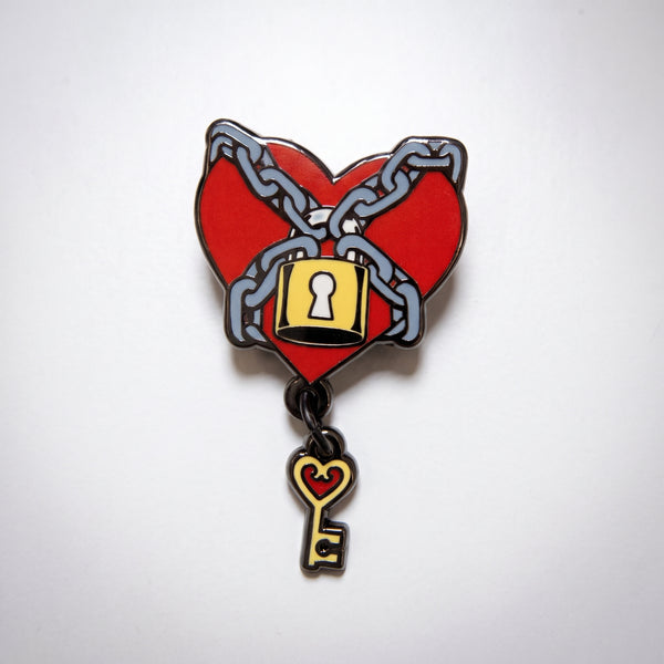 Chained Heart Key enamel pin, a red heart wrapped in gray chains and a yellow padlock with a heart-shaped key dangling below