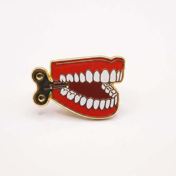 Chatter Teeth enamel pin, a pair of red wind-up chattering teeth with a gold key