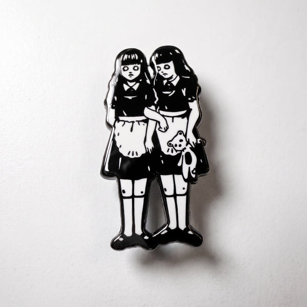 Creepy Twins enamel pin, two pale black-haired twin girls in matching black and white dresses, one holding a teddy bear
