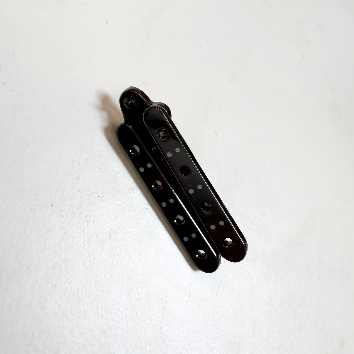 Black Butterfly Knife pin folded closed, the blade tucked between the two dotted black handles