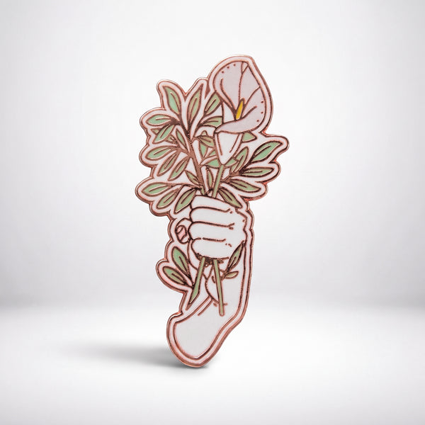 Hand With Flowers enamel pin, a pale hand holding a bouquet of white calla lilies and sage green leaves outlined in rose gold