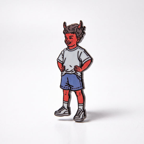 Little Devil Boy enamel pin, a grinning red-skinned boy with horns in a white tee, blue shorts and sneakers, hands on hips