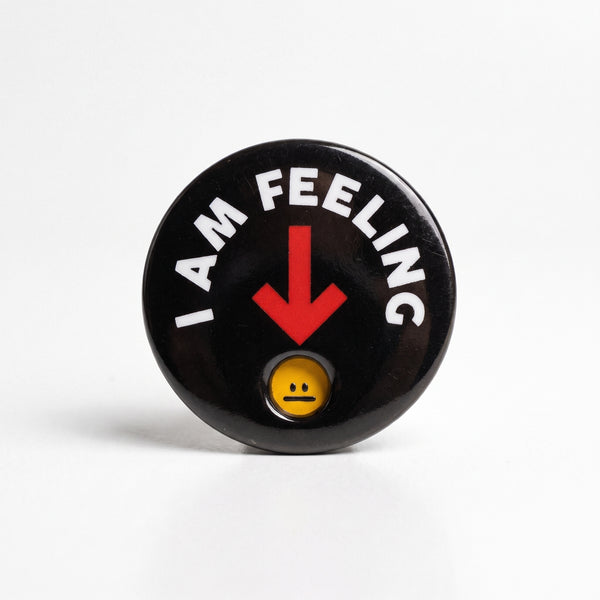 Mood Indicator enamel pin, a round black badge reading I Am Feeling with a red arrow pointing to a yellow face in a window
