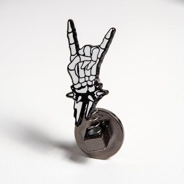 Skeleton Hand Bobble enamel pin, a white skeleton hand throwing rock-on horns with a spiked black cuff, mounted on a spring