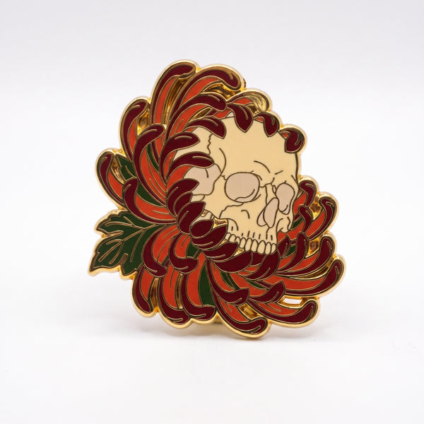 Skull Chrysanthemum enamel pin, a cream skull nestled in the curling petals of a dark red and orange chrysanthemum