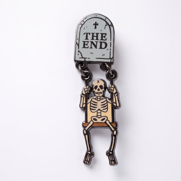 The End Skeleton enamel pin, a gray tombstone reading The End with a cream skeleton dangling below on a swing
