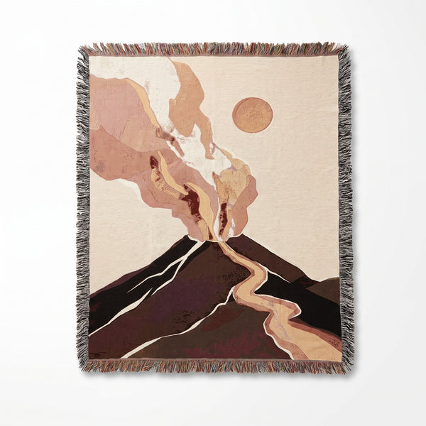 Volcano Eruption woven blanket showing a dark brown volcano pouring rivers of lava under billowing blush-pink smoke and a pale sun