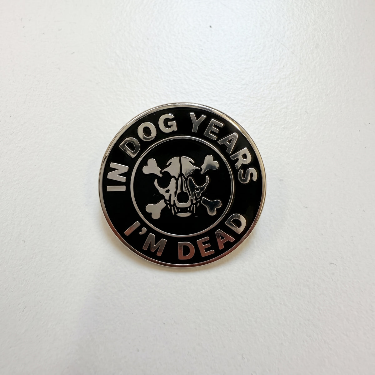 In Dog Years I'm Dead pin shown straight on, silver text around a dog skull and crossbones on black