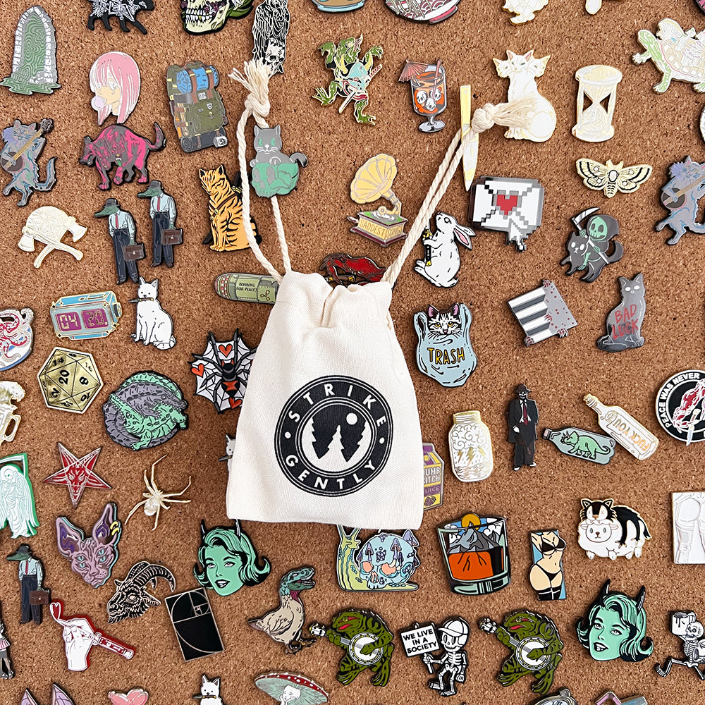 Strike Gently drawstring pouch surrounded by dozens of enamel pins on a corkboard