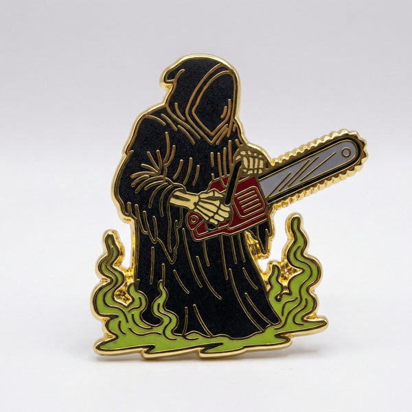 Enamel pin of Grim Reaper holding a red chainsaw with green fire at the base