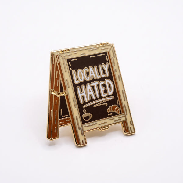 Locally Hated enamel pin, a gold-framed sidewalk chalkboard sign reading Locally Hated