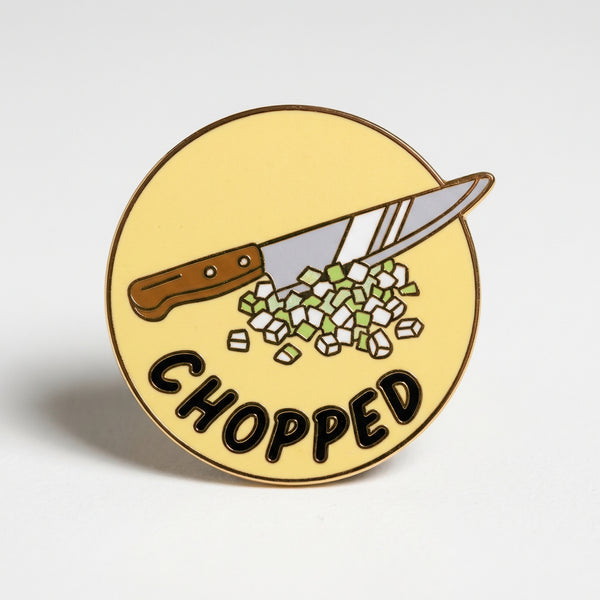 Circular enamel pin showing a chef knife chopping green onions on a yellow background with text CHOPPED