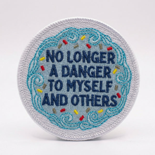Round embroidered patch with blue icing and sprinkles saying No Longer A Danger To Myself And Others