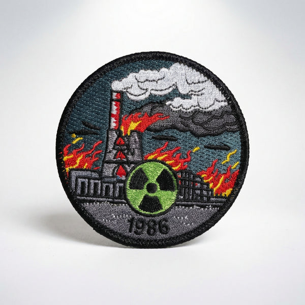 Circular embroidered patch featuring the burning Chernobyl nuclear plant, a green radiation symbol, and the date 1986.