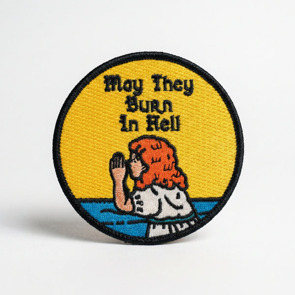 Round embroidered patch with a praying girl and text May They Burn In Hell on yellow background