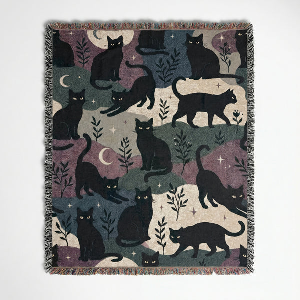 Woven tapestry blanket with black cats, crescent moons, and stars pattern with fringed edges