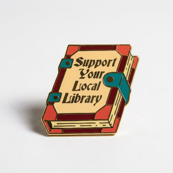 Enamel pin shaped like a vintage book reading Support Your Local Library