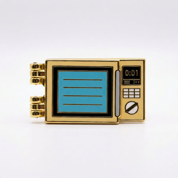 Gold enamel pin shaped like a microwave with a hinged door and 0:01 on the display