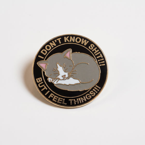 I Feel Things enamel pin, a curled up gray and white cat in a black circle reading I Don't Know Shit But I Feel Things