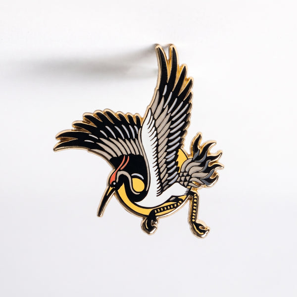 Japanese Crane enamel pin, a red-crowned crane with black and white wings swooping in front of a yellow sun