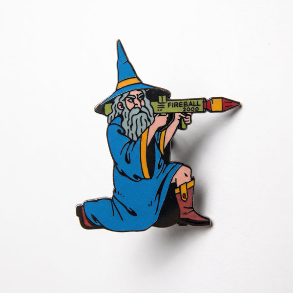 Fireball Wizard enamel pin, a gray-bearded wizard in a blue robe and hat aiming a green rocket launcher labeled Fireball