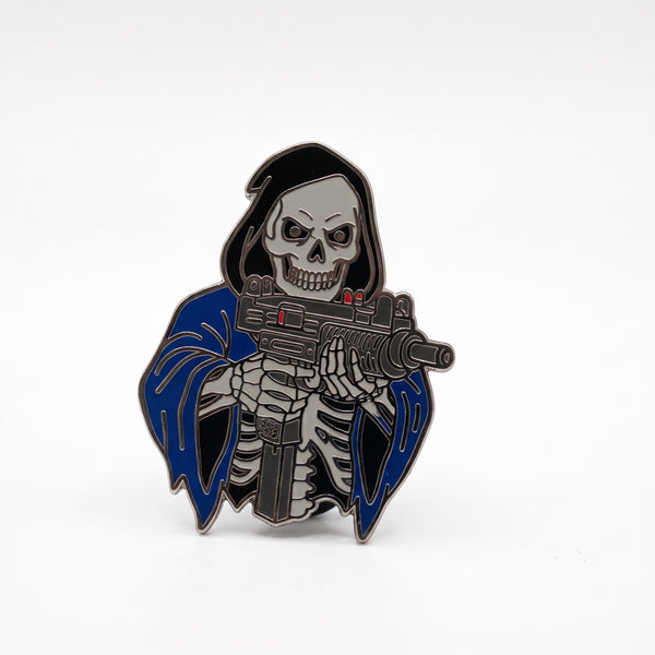 Uzi Reaper enamel pin, a hooded grim reaper skeleton in a black and blue cloak aiming a gray submachine gun