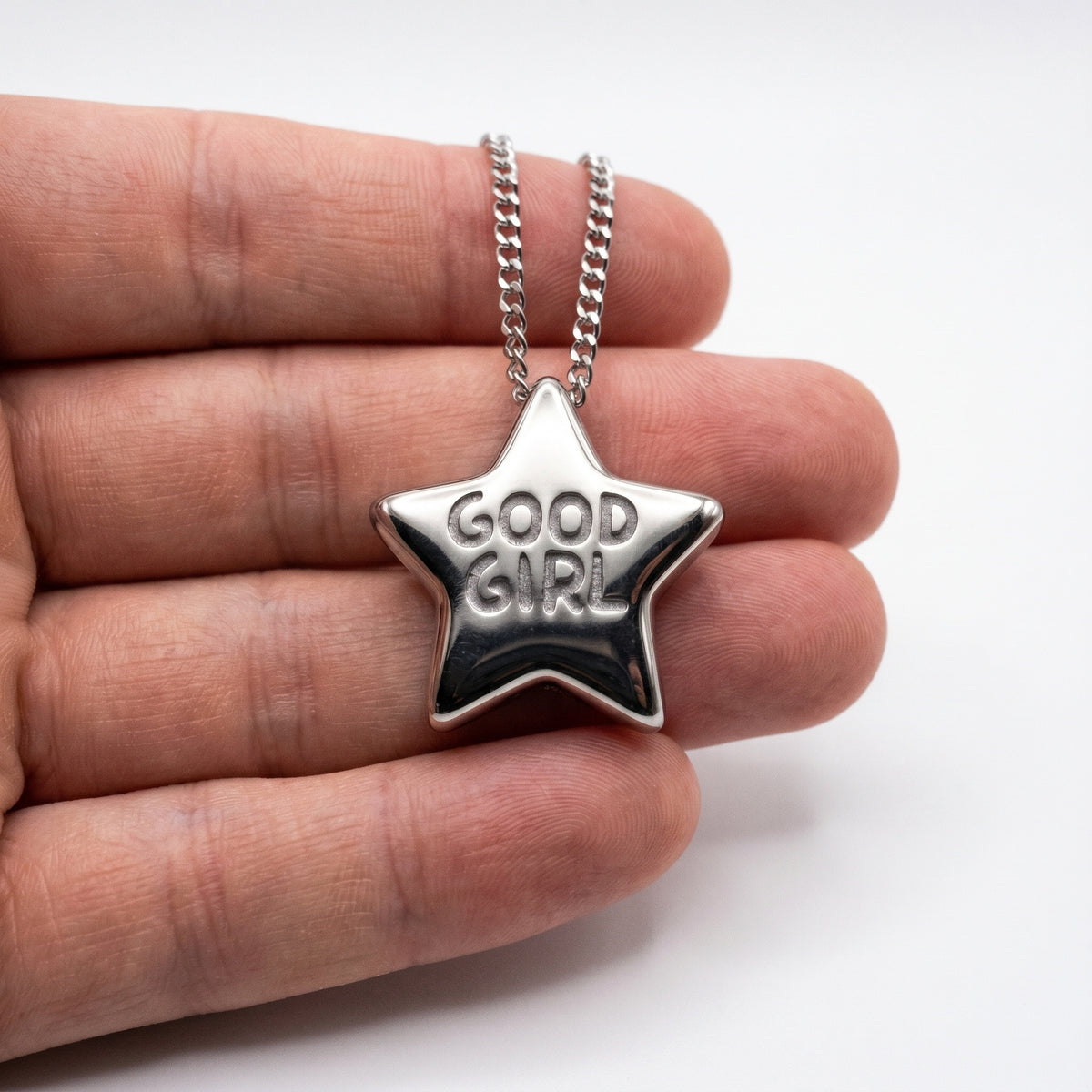 Close-up of the Good Girl pendant held in a hand, a puffy silver star stamped Good Girl on a curb chain