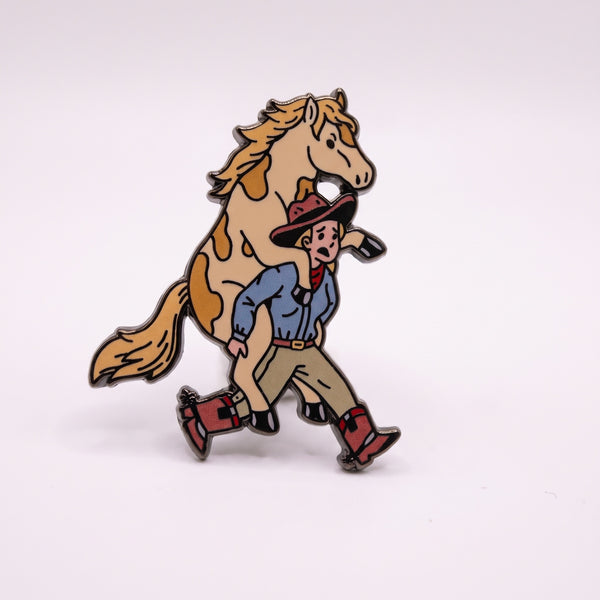 Horse Riding Cowboy enamel pin, a cream paint horse riding piggyback on a panicked cowboy in a blue shirt and red boots