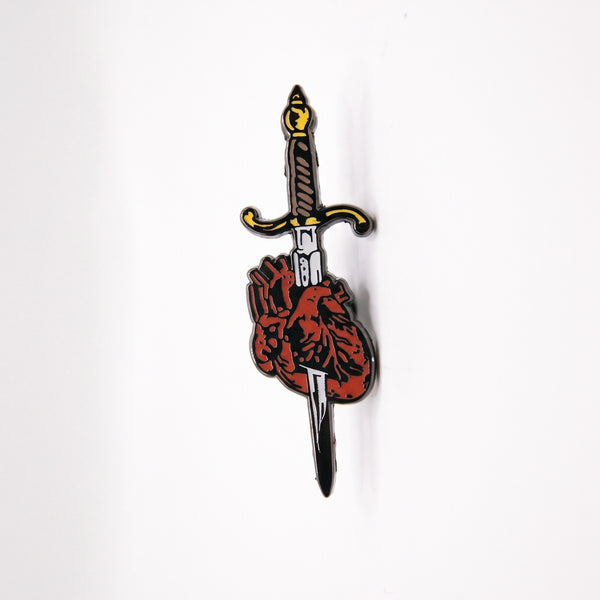 Stabbed Heart enamel pin, a dagger with a black and gold hilt plunged through a red anatomical heart